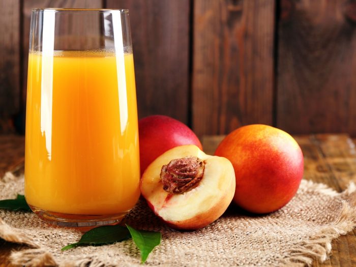 A glass with peach juice, with sliced and whole peaches on the side