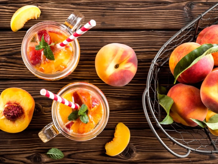 Two jars filled with cold peach tea or peach beverage surrounded by peach fruits