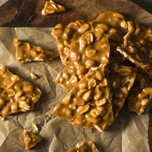 Peanut brittle pieces on a parchment paper placed on a wooden board