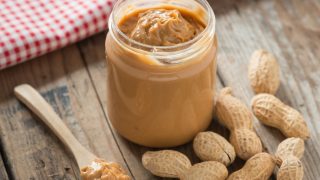 A spoonful of peanut butter and a handful of deshelled peanuts besides a jar of peanut butter