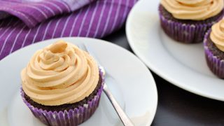 Peanut butter frosting on chocolate cupcakes on a white plate on a table with a purple napkin