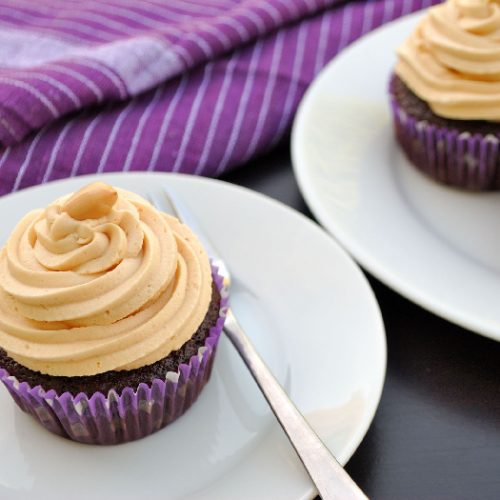 Peanut butter frosting on chocolate cupcakes on a white plate on a table with a purple napkin