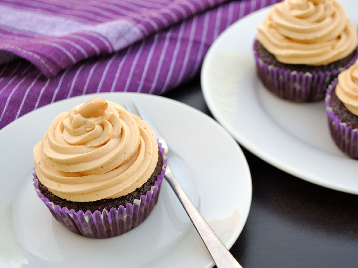 Peanut butter frosting on chocolate cupcakes on a white plate on a table with a purple napkin