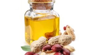Handful of peanut pods and peanuts besides a bottle of peanut oil closed with a cork