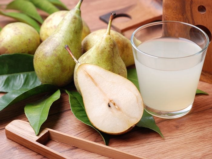 Pear juice in a glass surrounded by a couple of pears