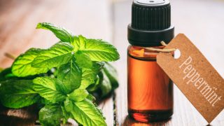 A bottle of peppermint oil with a fresh twig on a wooden table