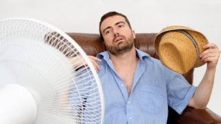 An exhausted man sitting in front of the fan with a hat in his hand
