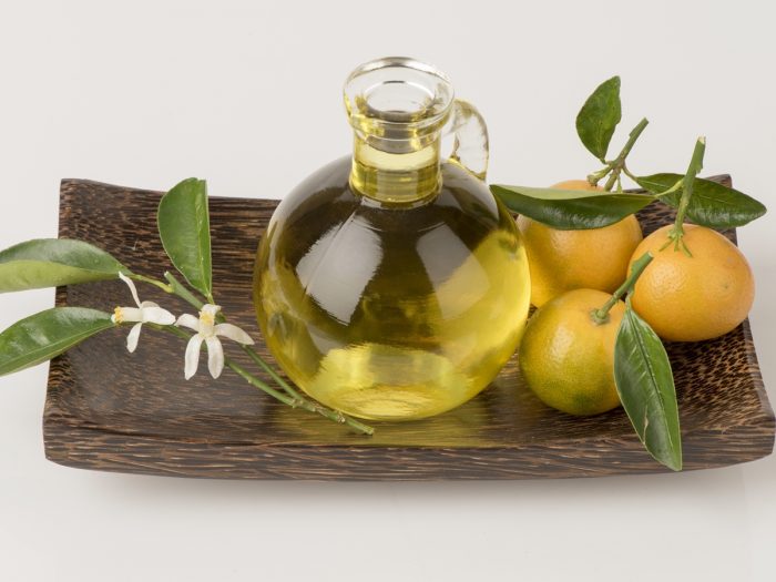 A close-up image of petitgrain essential oil and bitter oranges on a tray