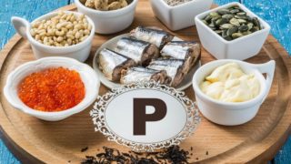 Foods rich in phosphorus (black tea, red caviar, pine nuts, peanuts, bran, sliced sardines, pumpkin seeds, & processed cheese) on a blue wooden table