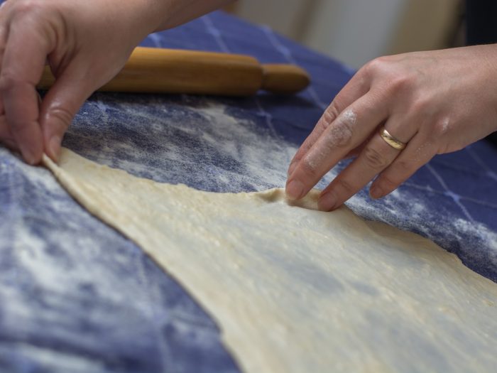 Woman's hands handling phyllodough on a wooden table with flour and a rolling pin on a table