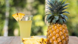 Close-up of a whole pineapple, two slices of pineapple and a glass of pineapple juice