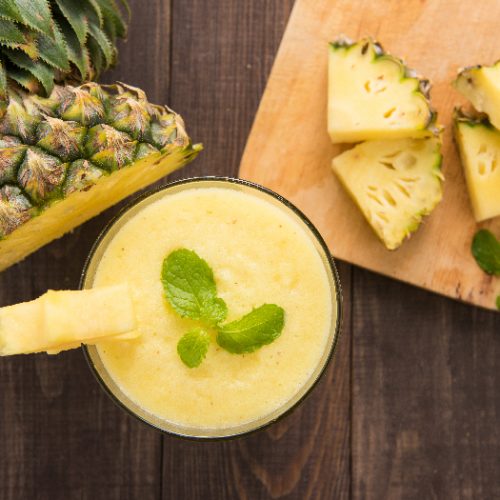 A flat lay pic of pineapple juice with fresh pineapple on a wooden table.