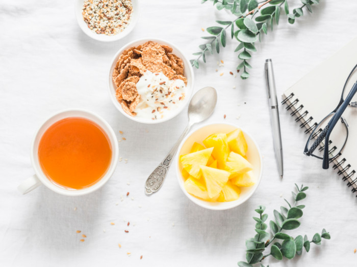 Three cups filled with pineapple, tea, and cereal on a white table