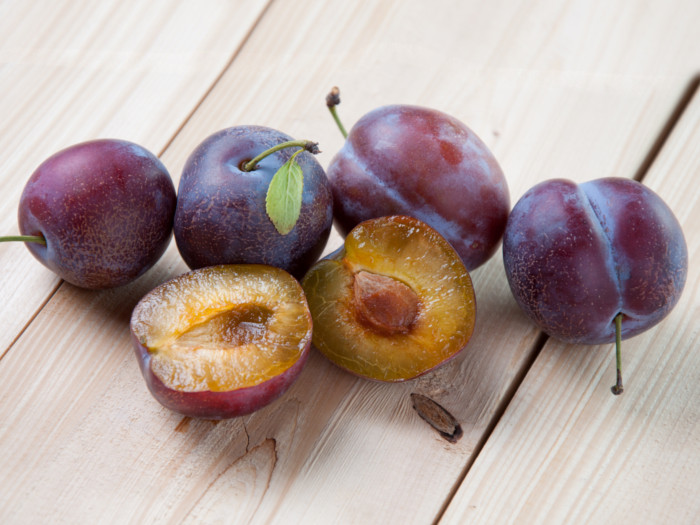 Close-up of fresh ripe whole and halved pluots on a wooden table