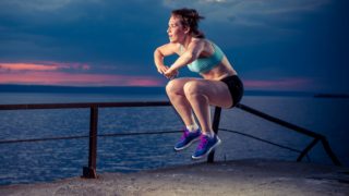 A woman in gym clothes practicing plyometric exercises outdoors against a sunset