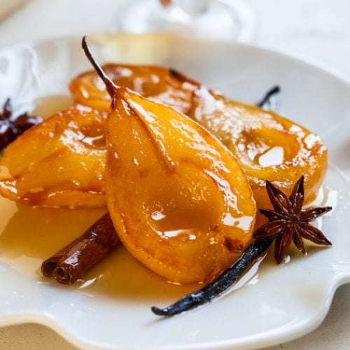 Poached pears with spices in syrup on a white plate