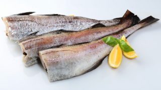 Raw deboned pollock fish with lime wedges and herbs