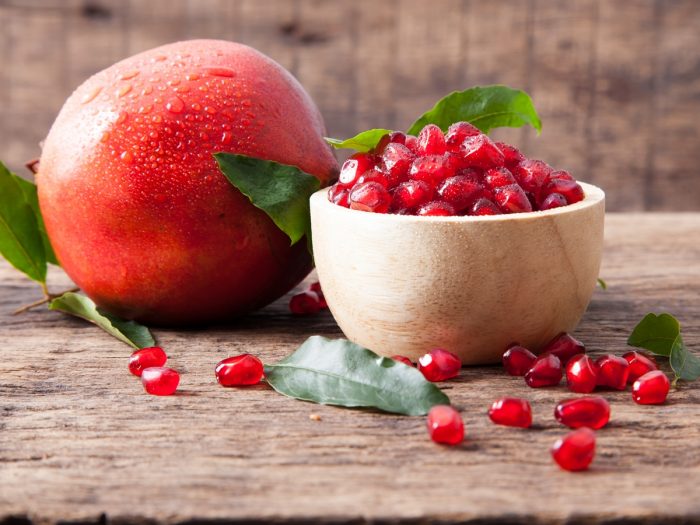 Fresh pomegranate seeds in a bowl with a whole pomegranate fruit aside