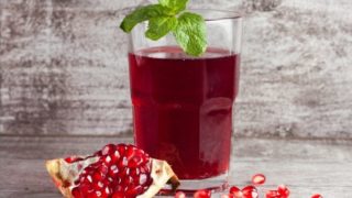 A glass of pomegranate juice and seeds on a wooden background.