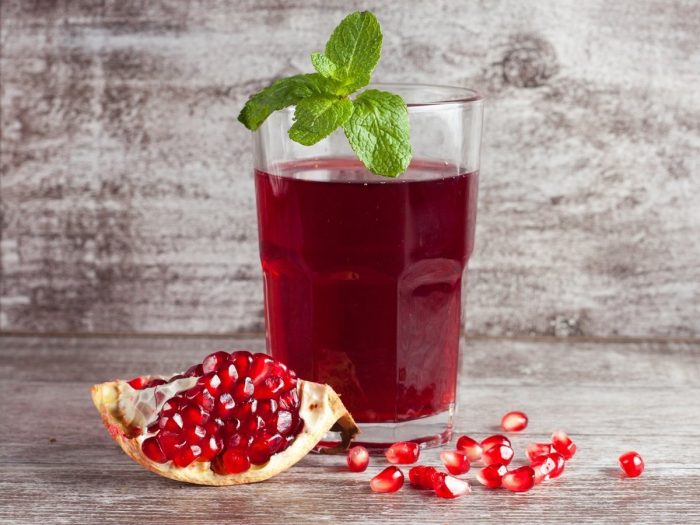 A glass of pomegranate juice and seeds on a wooden background.