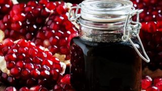 A jar filled with pomegranate molasses on a bed of pomegranate seeds