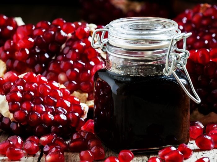 A jar filled with pomegranate molasses on a bed of pomegranate seeds