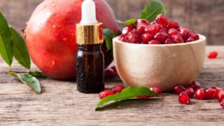 Fresh bowl of pomegranate seeds, bottle of oil, and whole pomegranate fruit on a table