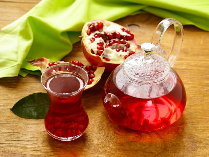 A small kettle and tea cup filled with pomegranate tea and two halves of pomegranates around