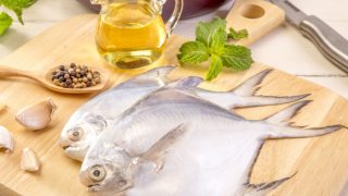 Pompano fish on a wooden cutting board with an oil bottle and spices in the background