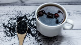 A cup of poppyseed tea kept beside a spoon containing poppy seeds