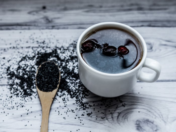 A cup of poppyseed tea kept beside a spoon containing poppy seeds