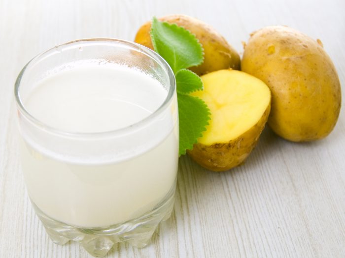 A glass of potato juice and whole and halved potatoes on a wooden table