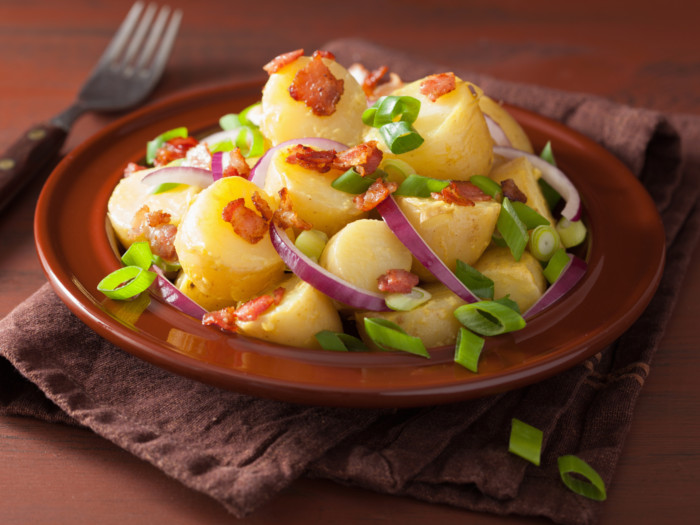 bowl of potato salad topped with spring onions and bacon