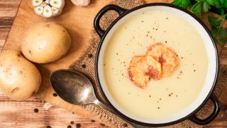 Homemade potato cream soup with potato chips, kept next to potatoes, on a wooden table
