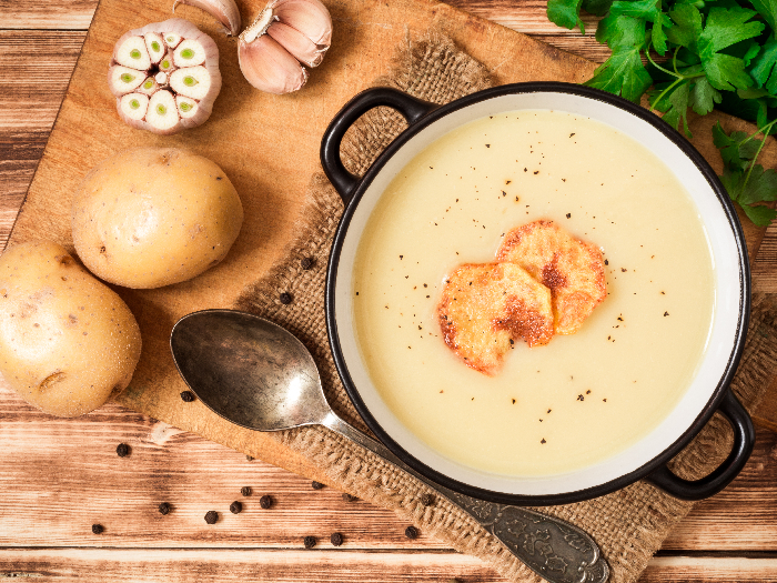 Homemade potato cream soup with potato chips, kept next to potatoes, on a wooden table