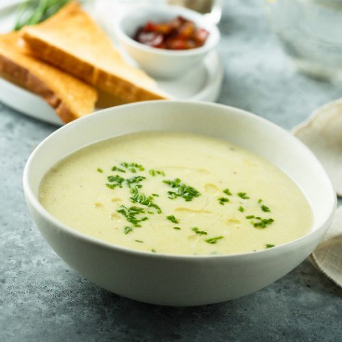 Homemade potato cream soup kept in a white bowl atop a bluish grey platform