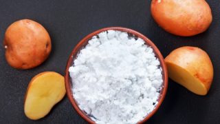 A cup of potato starch surrounded by potatoes