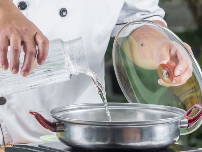 A chef pouring water in a pan