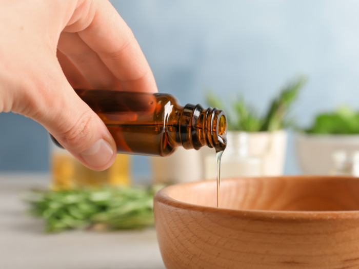 Hand pouring oil into a wooden bowl.