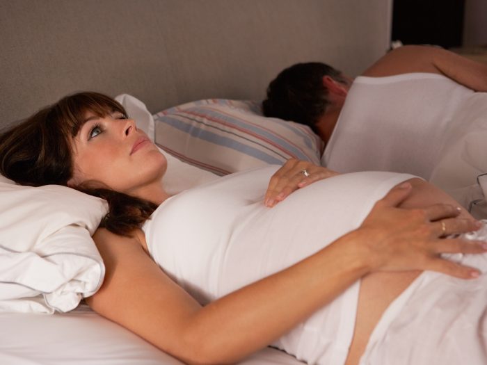 Pregnant woman lying awake in bed with a sleeping man beside her