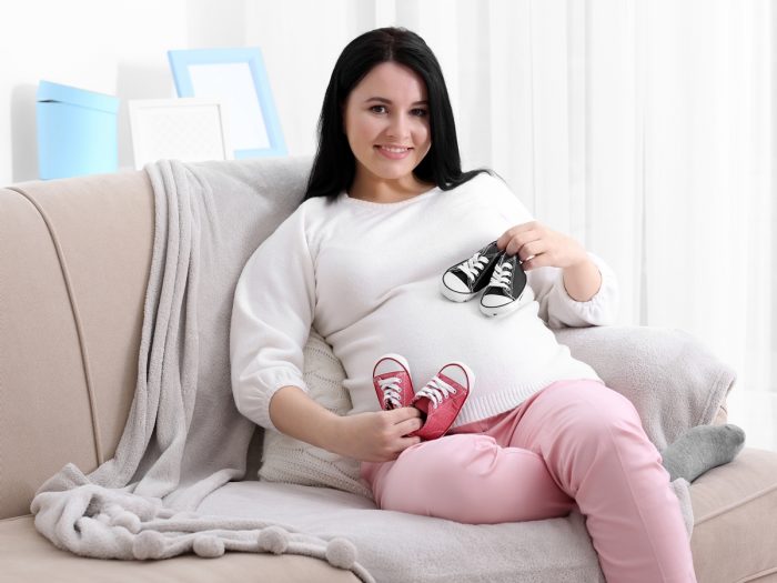 A pregnant woman sitting on a couch with baby shoes in both her hands