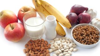 Probiotic bottle, almonds, beans, apples, bananas, and onions on a white background