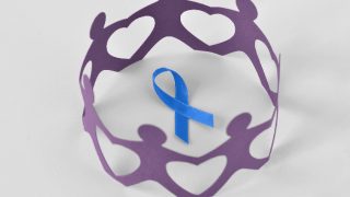 Paper people in a circle around blue ribbon on white background