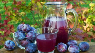 Prune juice in the carafe and glass with plums natural background in sunny day