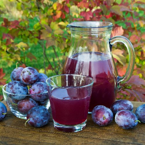 Succo di prugna in caraffa e vetro con prugne sfondo naturale in giornata di sole