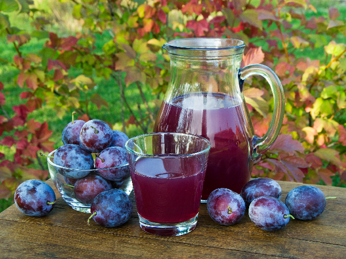 Succo di prugna in caraffa e vetro con prugne sfondo naturale in giornata di sole