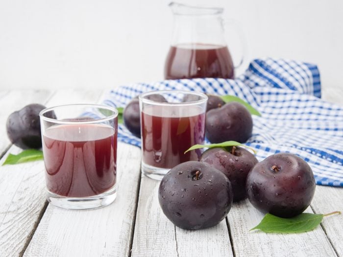 Two small glasses of prune juice surrounded by a couple of prunes and a huge jug full of prune juice