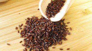 A small heap of ispaghula on a wooden surface with a scoop of more seeds.