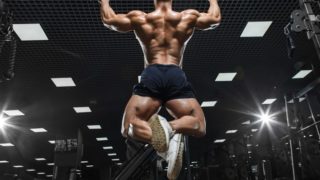Back view of a man in shorts doing pull-ups in a gym.