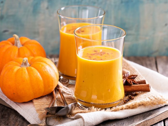 Two glass jars filled with pumpkin juice kept atop a table next to pumpkins